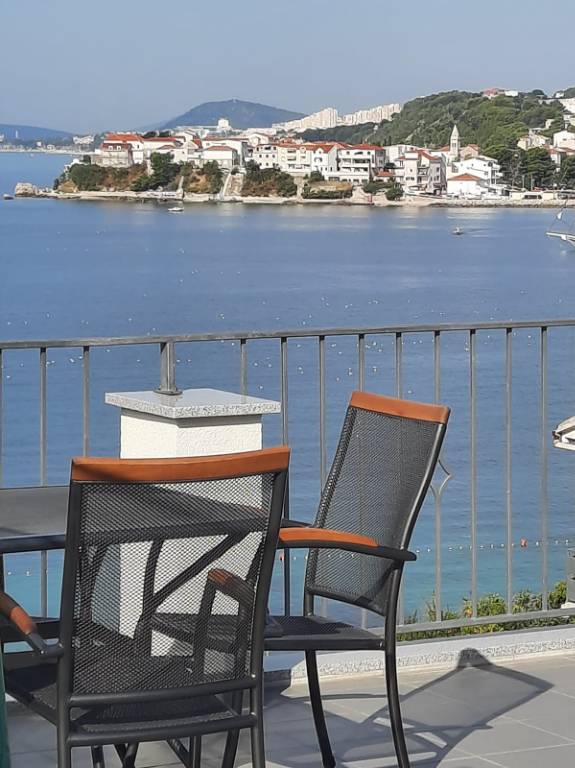 Terrasse mit Meerblick, ausgestattet mit Grill, Tisch, Stühlen, Sonnenschirm.